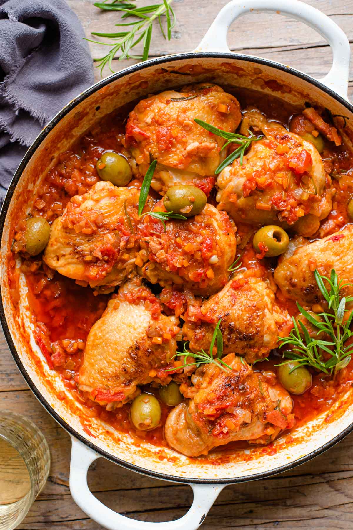 An overhead shot of chicken cacciatore in a large white casserole dish on a wooden background