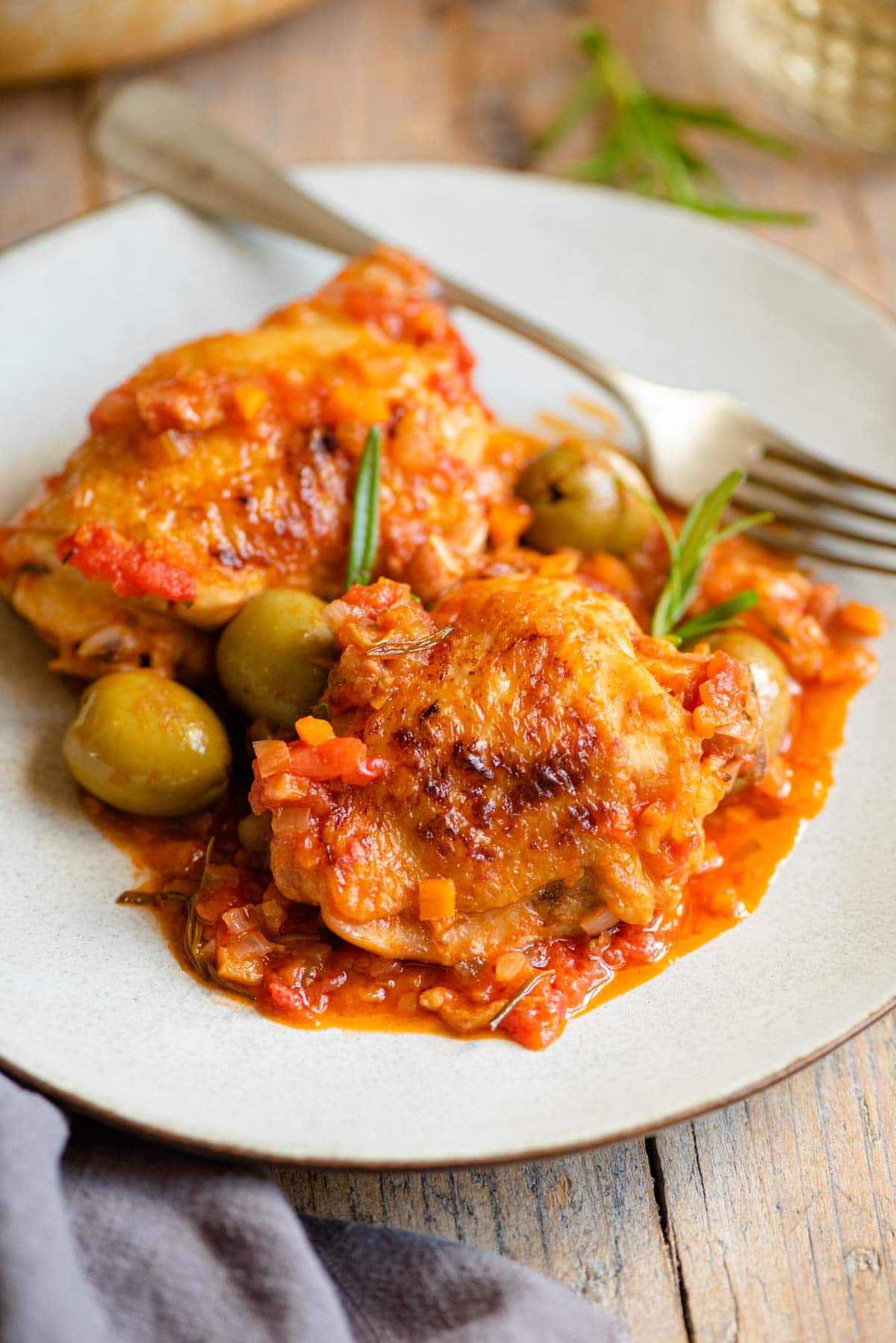 Two chicken thighs on a plate with a tomato and vegetable sauce and olives