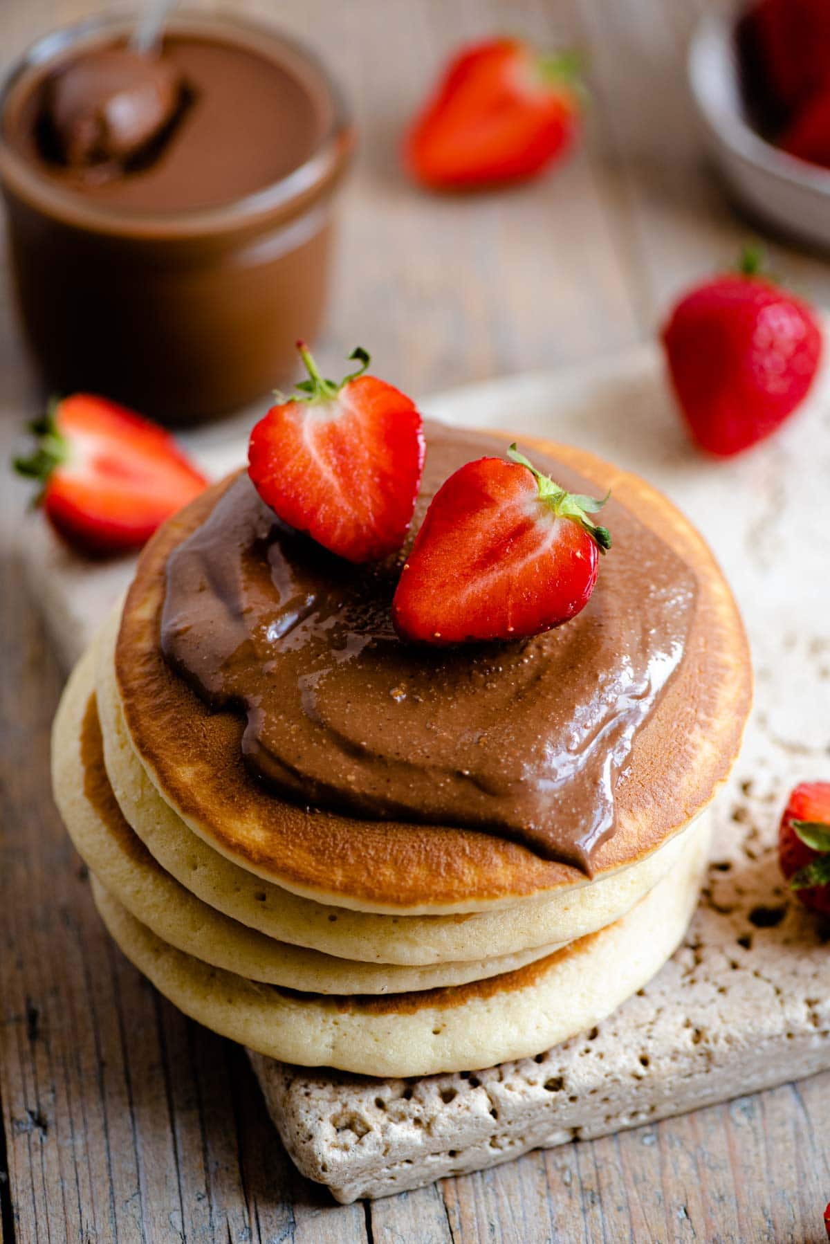 A close up of a stack of pancakes topped with Nutella and strawberries