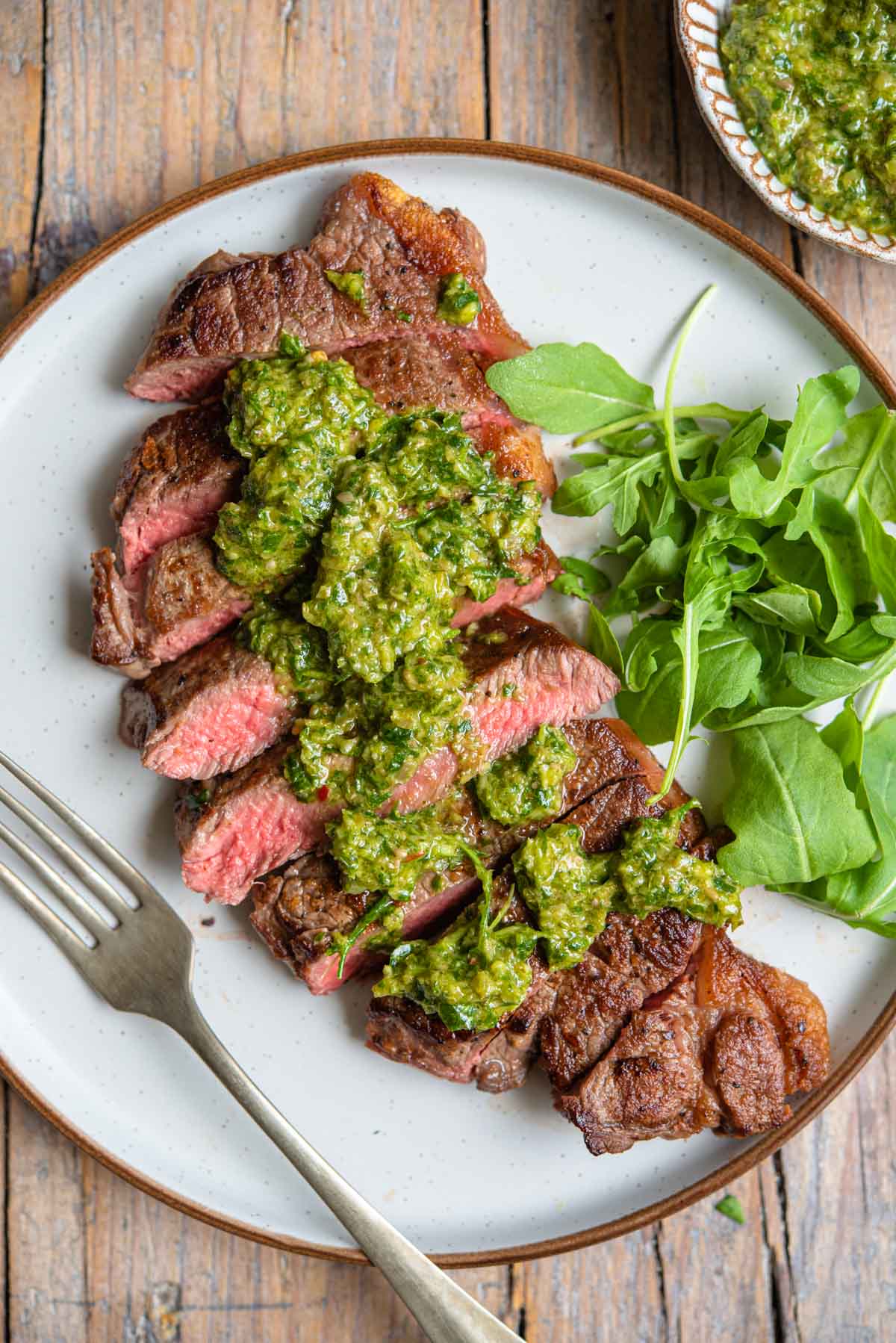 An overhead shot of steak cut into slices with Italian salsa verde on top