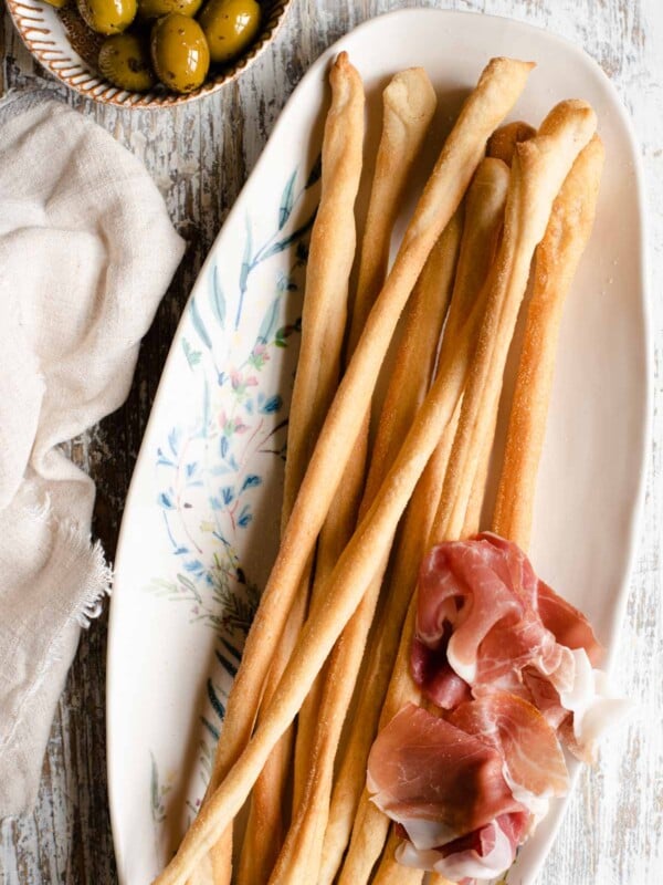 An overhead shot of Italian Grissini on a serving plate with olives at the side