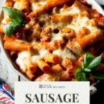 A cheesy bake sausage pasta bake in an oval dish with a text overlay that reads; Sausage Pasta Bake - Spicy and Creamy.