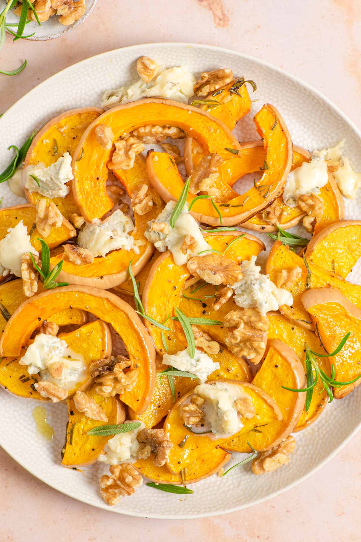 An overhead shot of roasted butternut squash on a serving plate with gorgonzola and walnuts