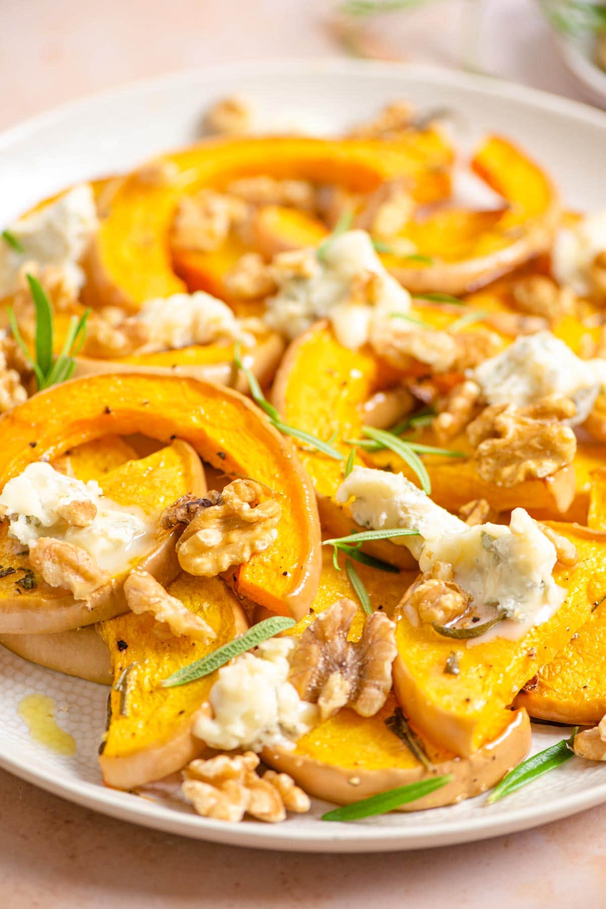 A close up of butternut squash on a serving plate with gorgonzola and walnuts