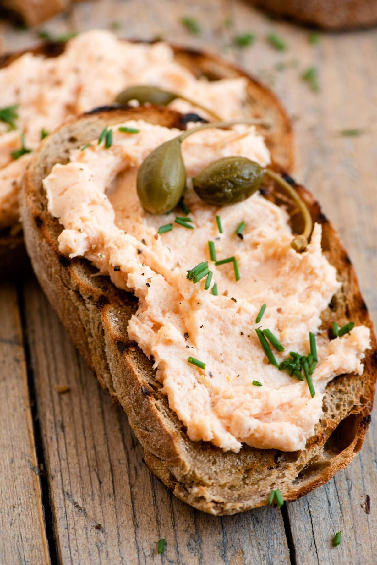 A close up of a slice of bread topped with smoked salmon pate, chives and capers.