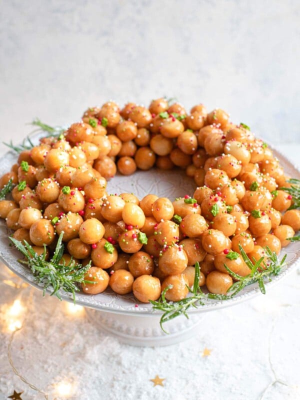 A side shot of Italian struffoli (honey balls) on a cake stand topped with sprinkles