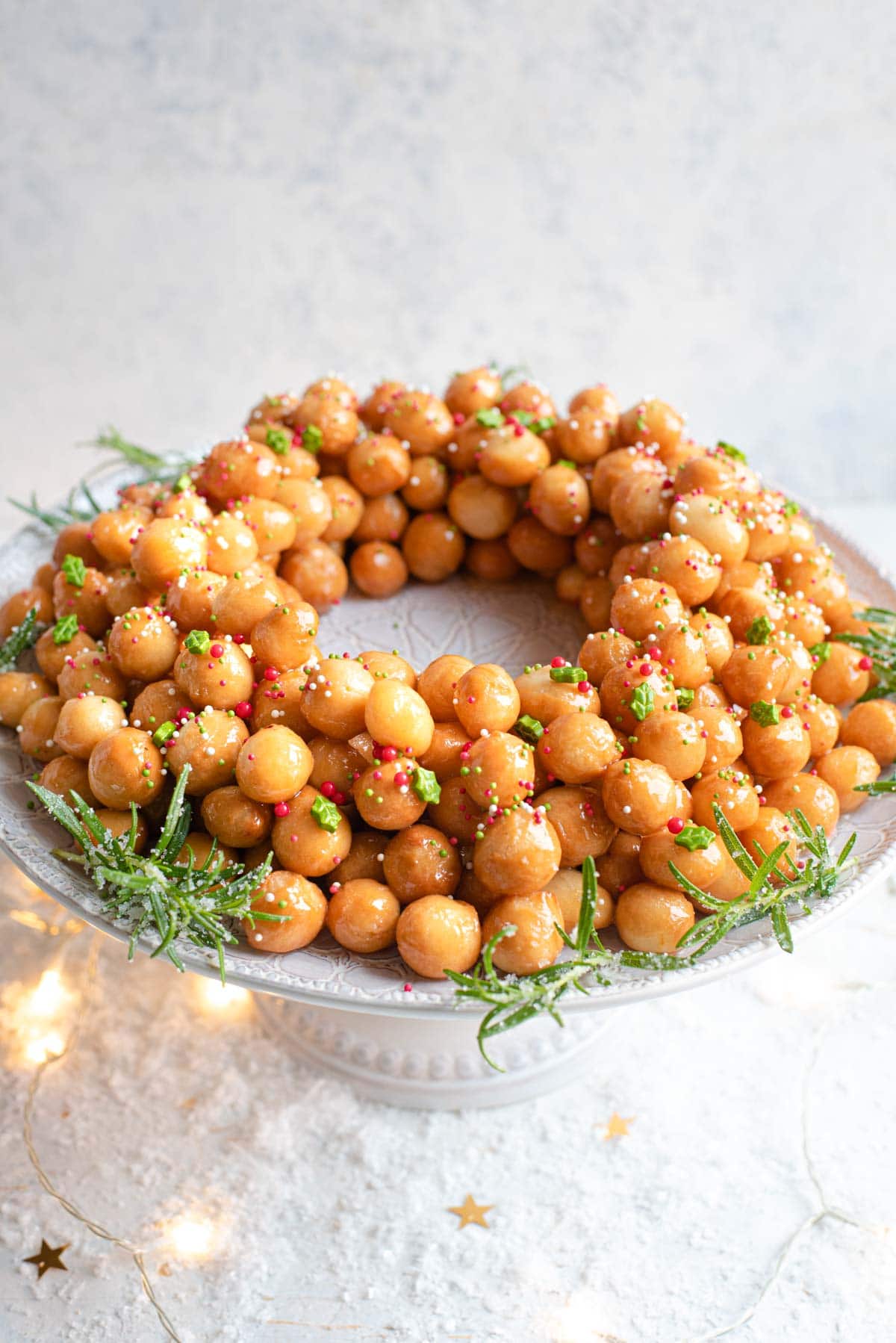 A side shot of Italian struffoli (honey balls) on a cake stand topped with sprinkles