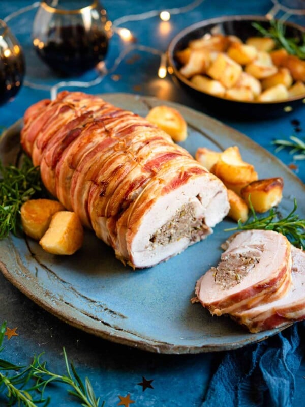 A stuffed turkey breast on a serving plate with slices cut and roasted potatoes