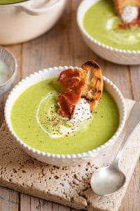 Green pea soup in a bowl topped with yogurt and crispy prosciutto