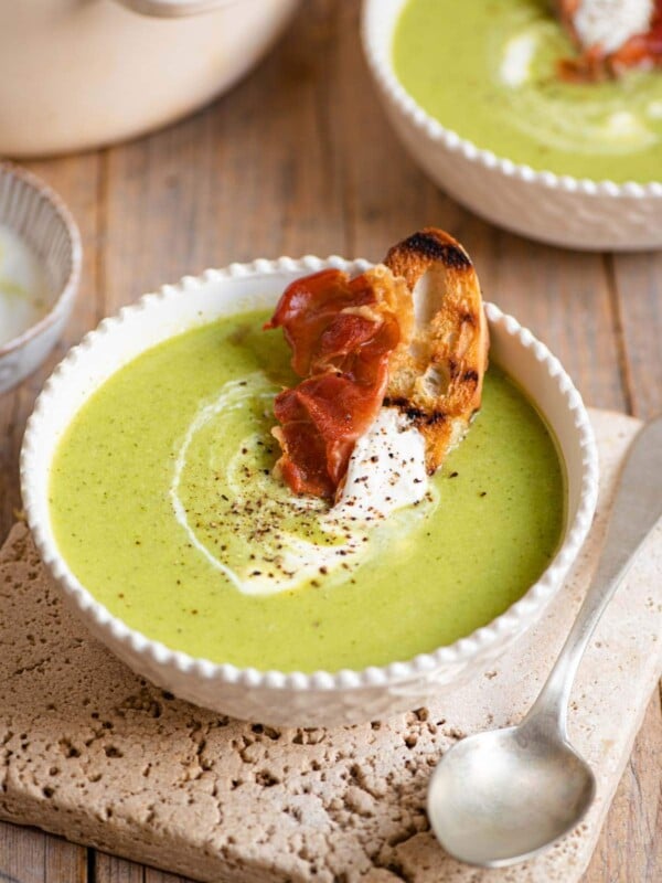 Green pea soup in a bowl topped with yogurt and crispy prosciutto