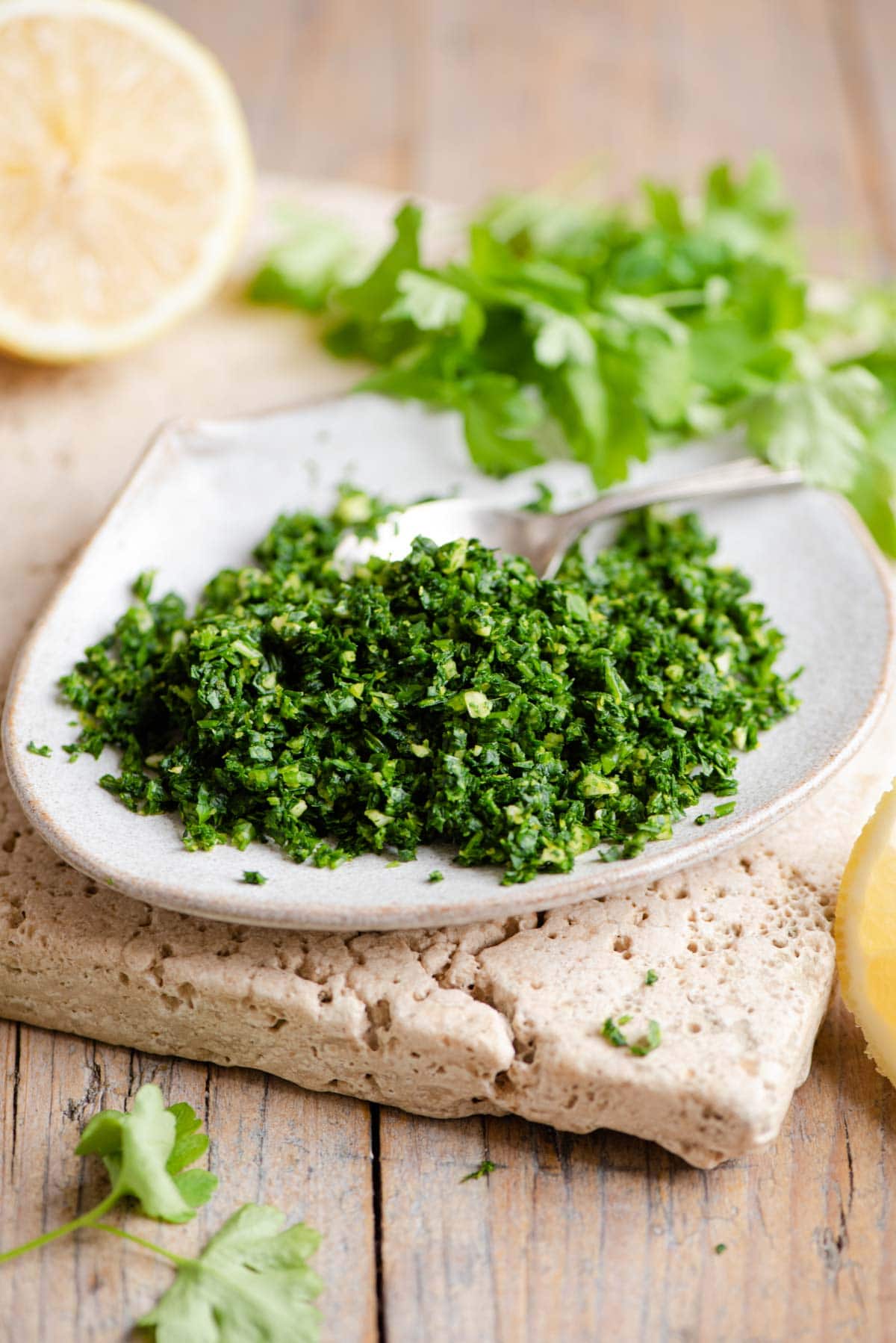 Gremolata on a small plate with wedges of lemon and parsley in the background