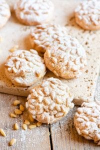 Pignoli cookies on a wooden surface dusted with powdered sugar