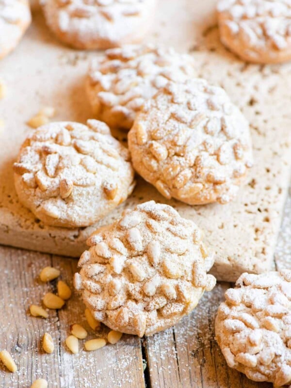 Pignoli cookies on a wooden surface dusted with powdered sugar