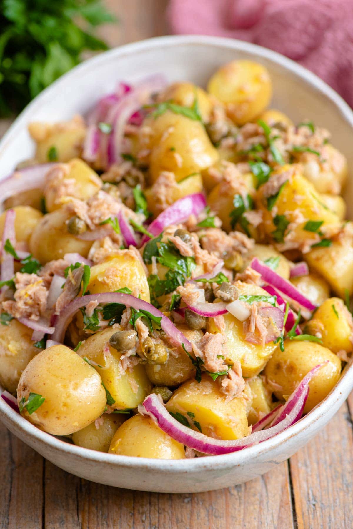 A close up of a tuna potato salad with red onion and capers in a bowl