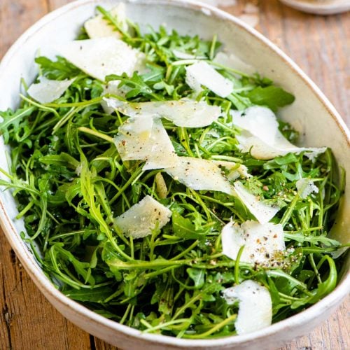 An arugula salad in a large serving bowl with shavings of parmesan