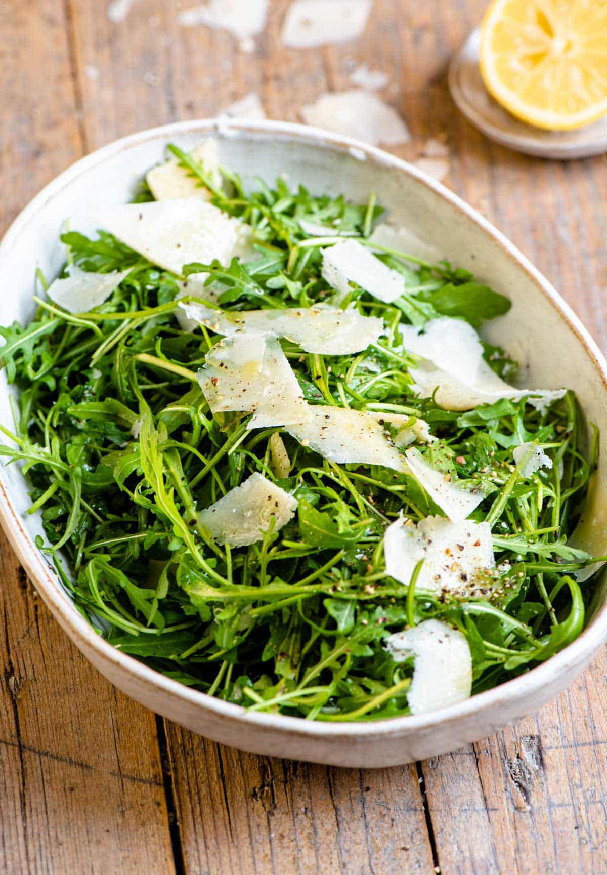 An arugula salad in a large serving bowl with shavings of parmesan