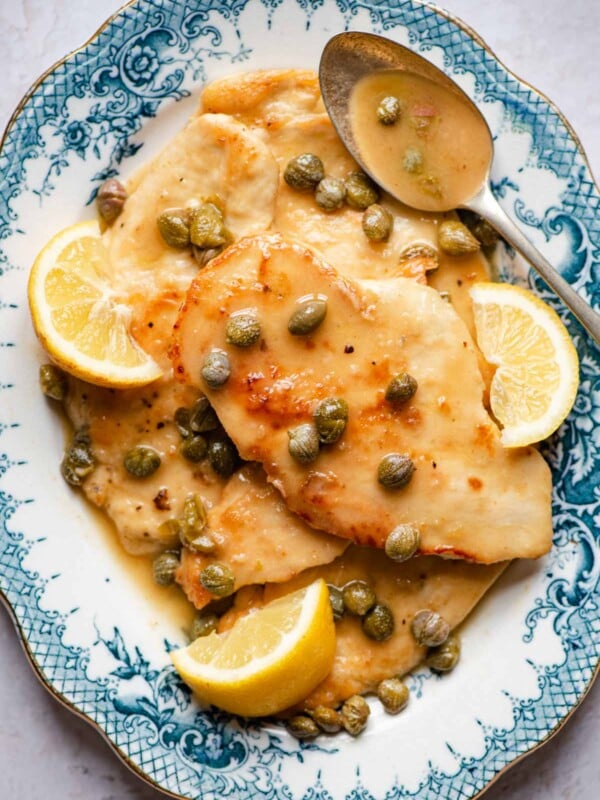 An overhead shot of chicken piccata on a blue serving plate with lemon wedges and capers