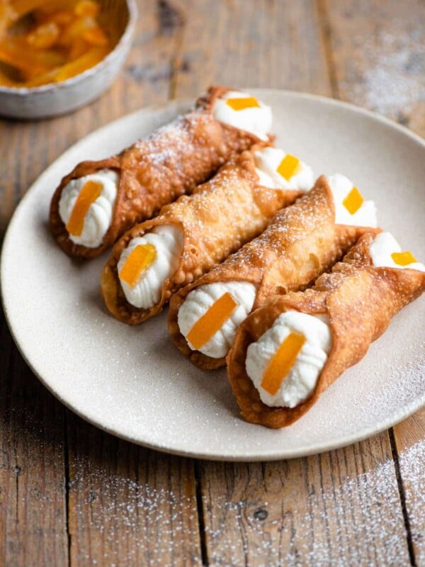 Four cannoli on a plate filled with ricotta and a slice of candied orange