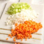 A close up of finely chopped carrot, celery and onion on a cutting board