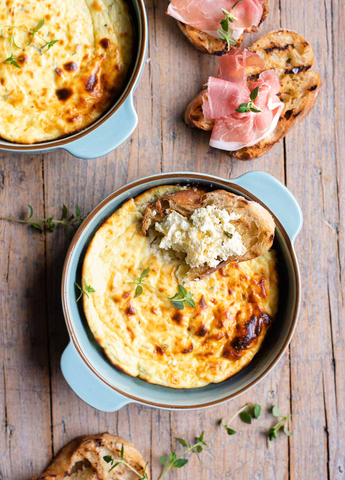 An overhead shot of baked ricotta in a blue dish with toasted bread at the side