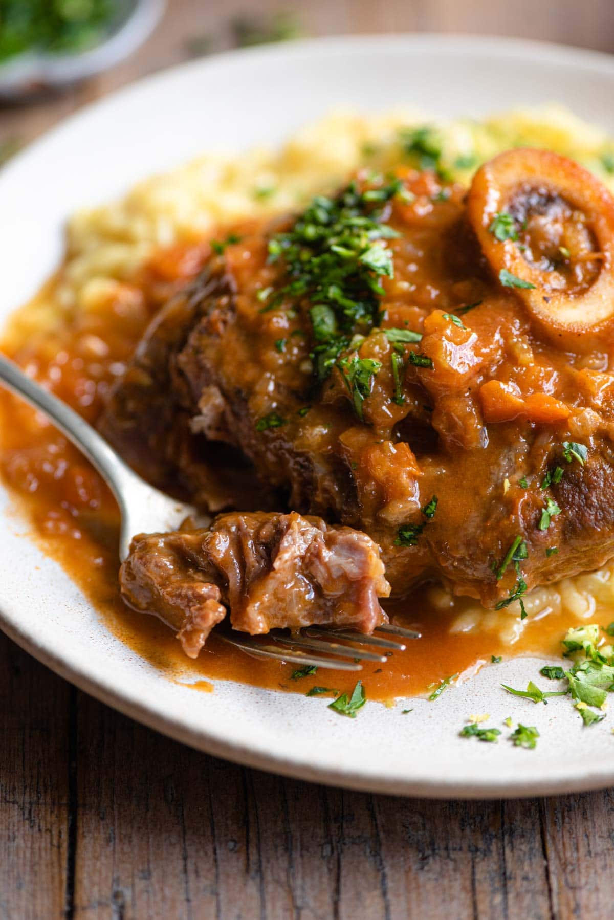 A close up of a piece of osso bucco on a fork with sauce