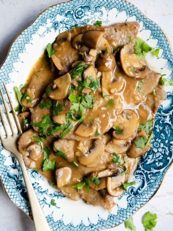 An overhead shot of veal marsala on a blue platter with mushrooms and parsley