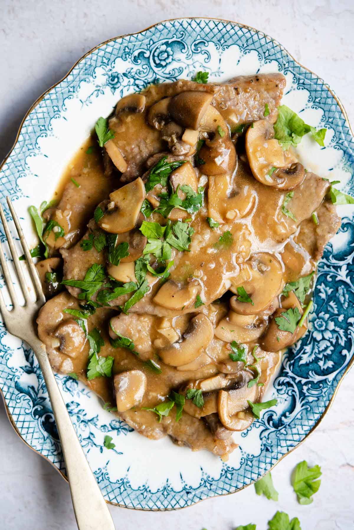 An overhead shot of veal marsala on a blue platter with mushrooms and parsley