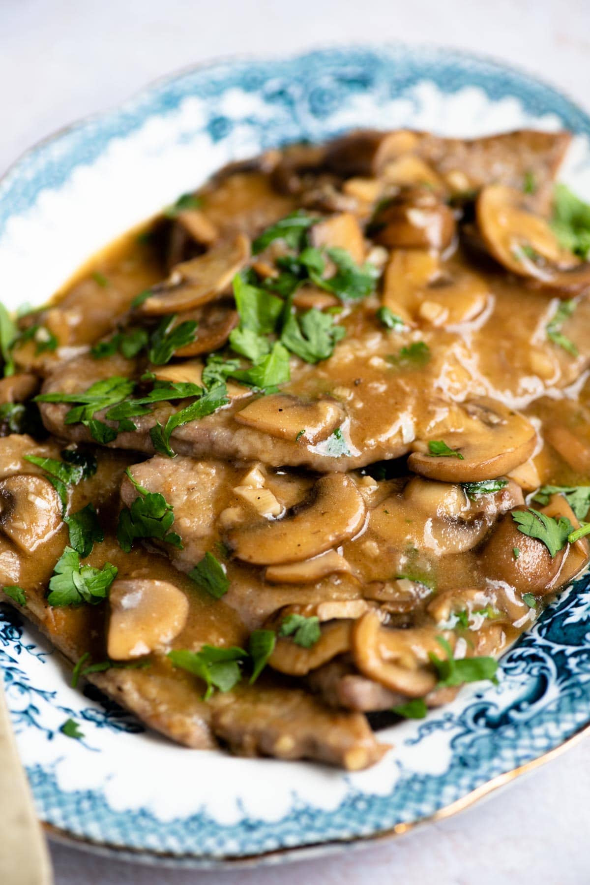 A close up of veal marsala with lots of sauce, mushrooms and parsley
