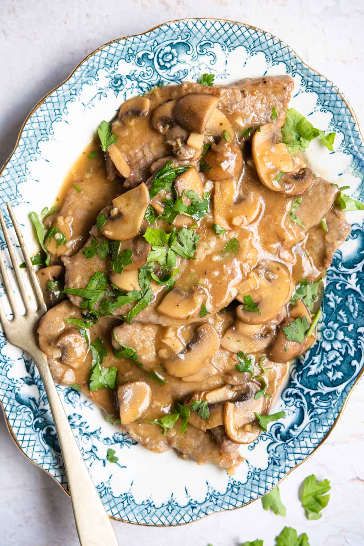 An overhead shot of veal marsala on a blue platter with mushrooms and parsley