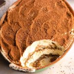 A close up of a dish of tiramisu with a scoop missing