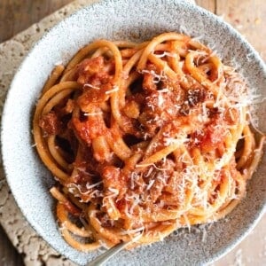 A close up of bucatini pasta in a bowl with amatriciana sauce