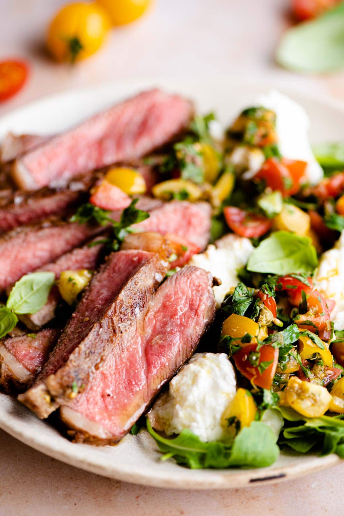 A close up of steak tagliata on a plate with tomato and mozzarella