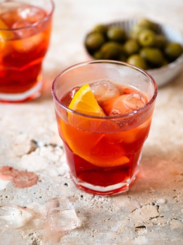 An Americano cocktail on a marble work surface with olives in the background