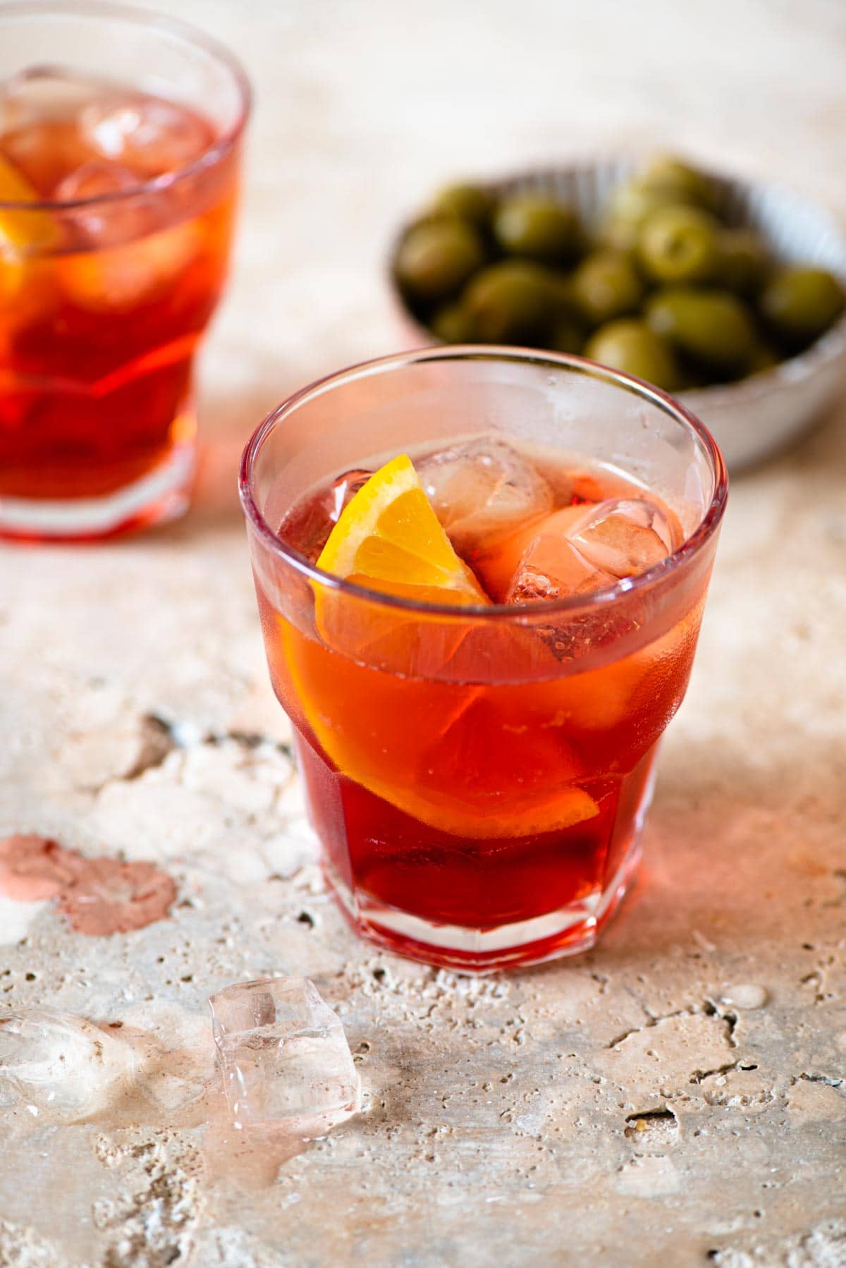 An Americano cocktail on a marble work surface with olives in the background