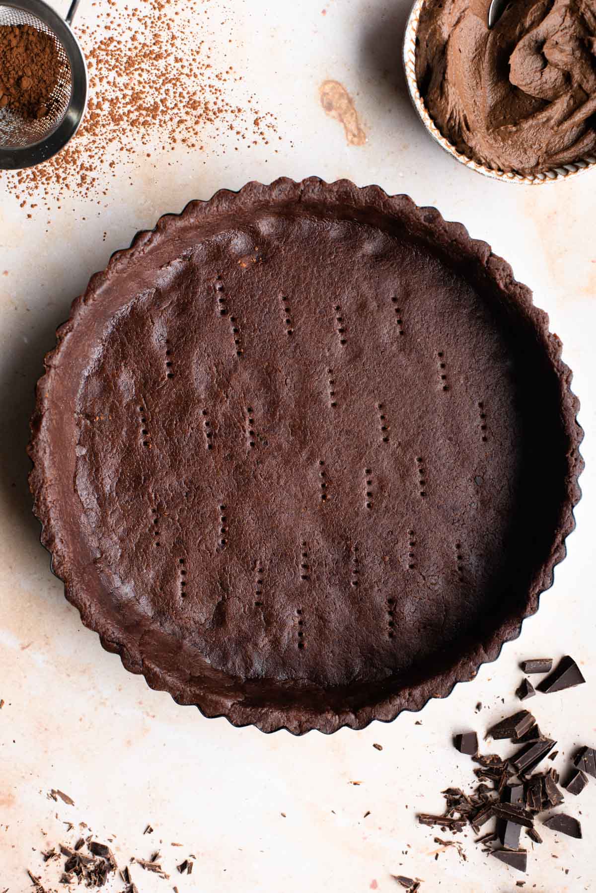 Unbaked chocolate shortcrust pastry in a tart pan sitting on a warm marble effect background