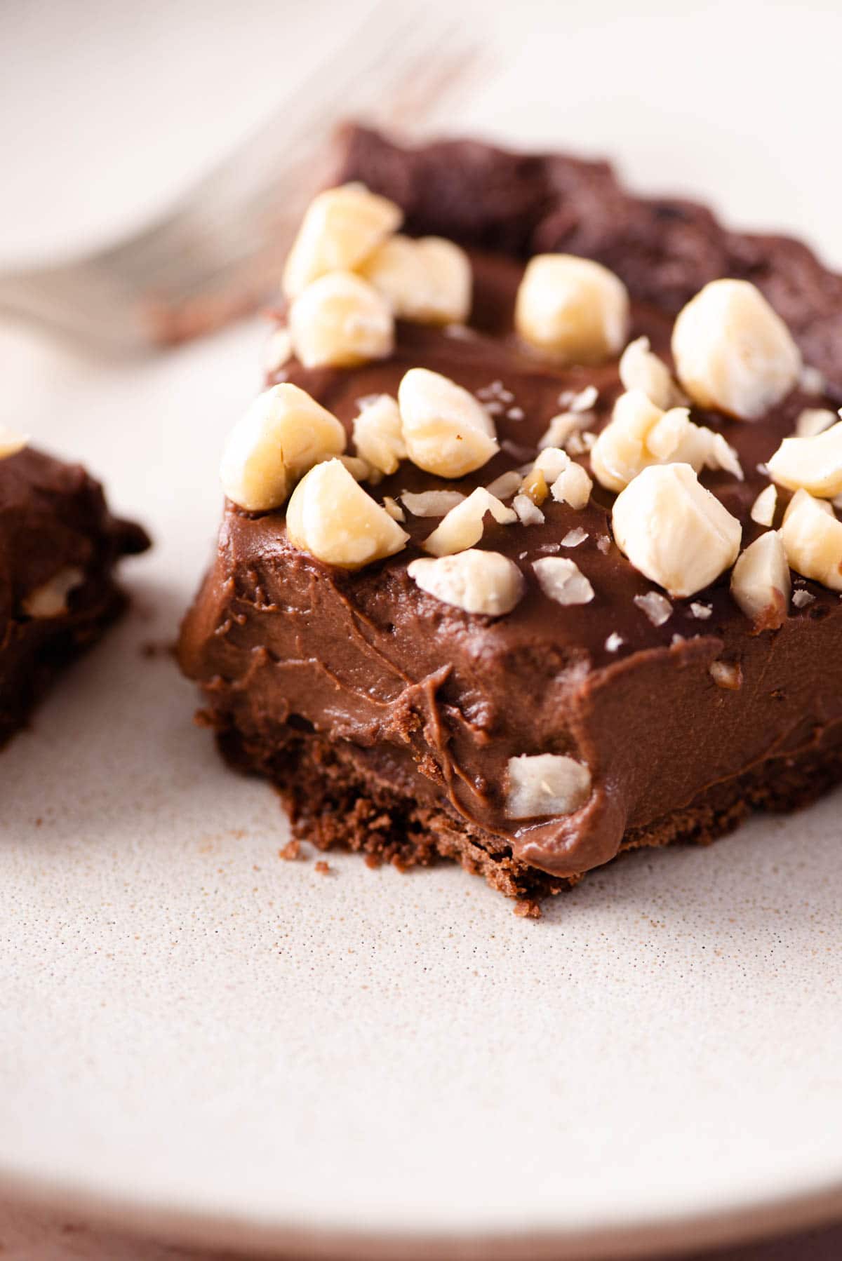 A close up of a slice of chocolate tart on a plate topped with hazelnuts