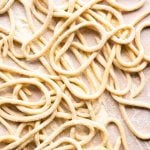 A close up of pici pasta on a neutral background