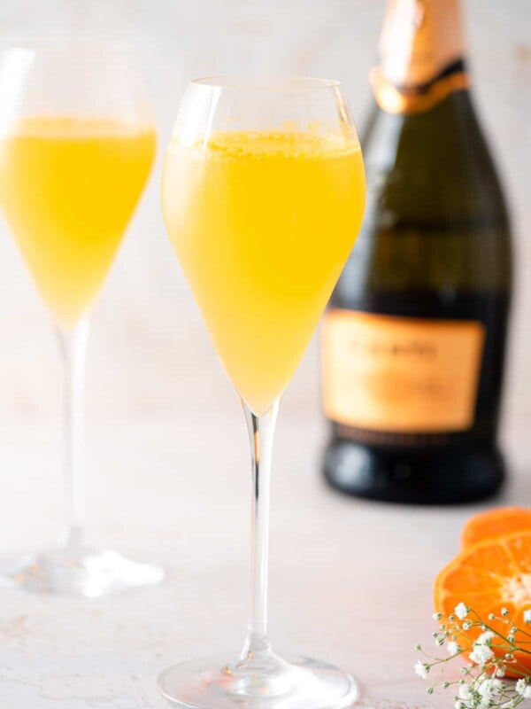 Two Puccini cocktails in flute glasses with a bottle of prosecco in the background