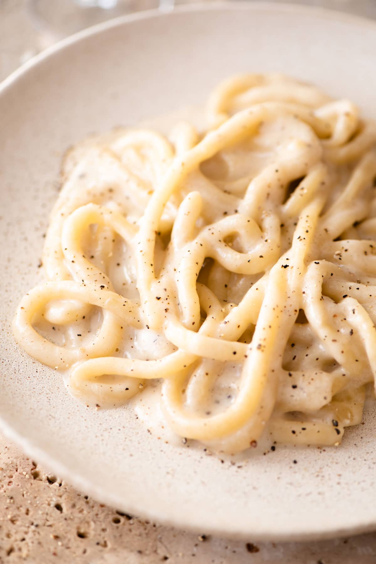 A close up of pici pasta with cacio e pepe sauce on a plate