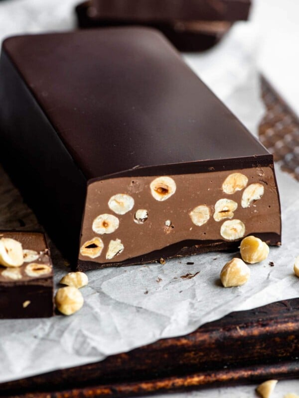 A chocolate torrone bar filled with hazelnuts sitting on baking parchment