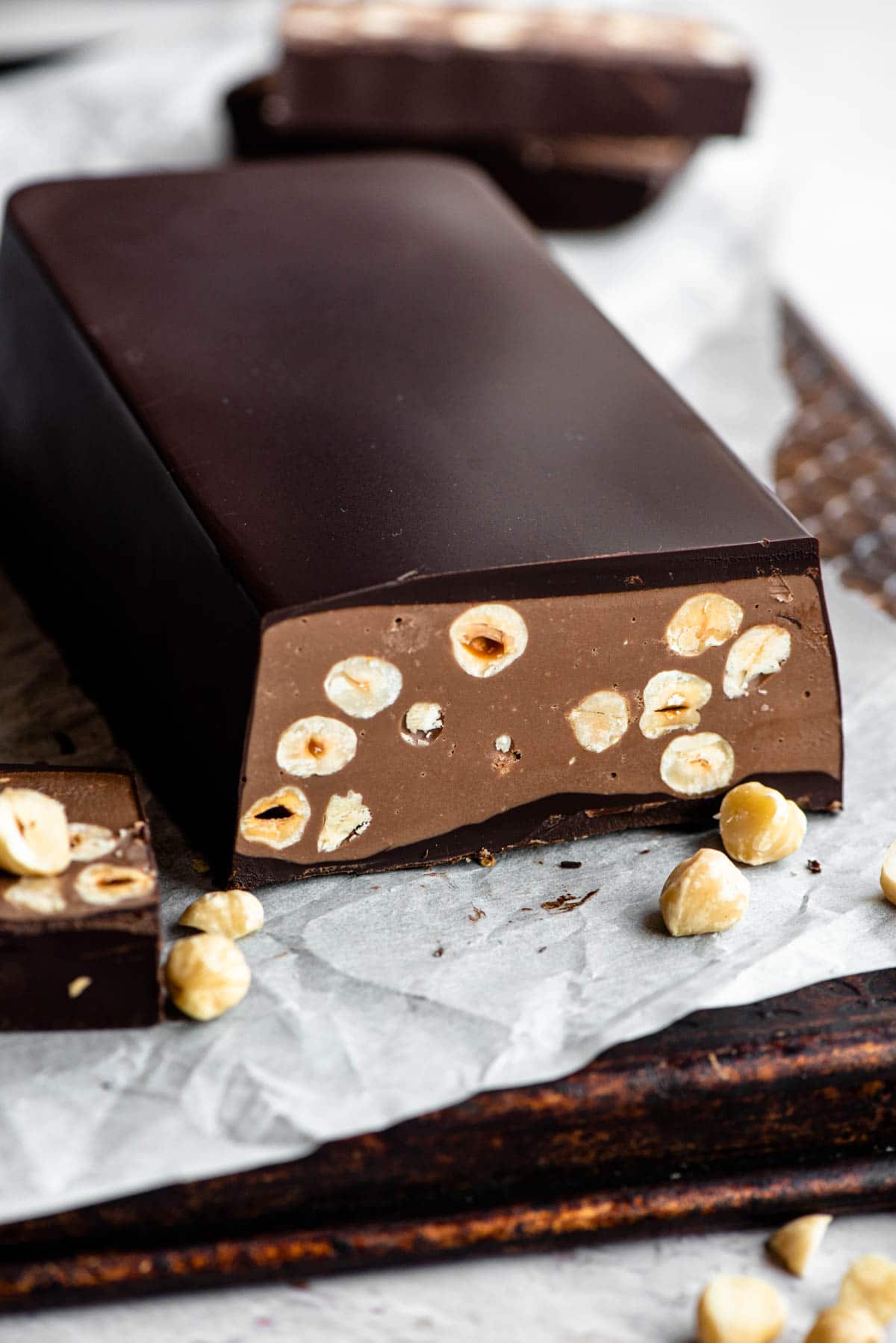 A chocolate torrone bar filled with hazelnuts sitting on baking parchment