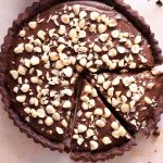 A close up of a chocolate tart topped with chopped hazelnuts