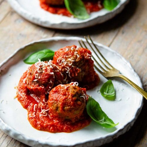 Polpette (Italian meatballs) in a tomato sauce on a plate topped with basil.