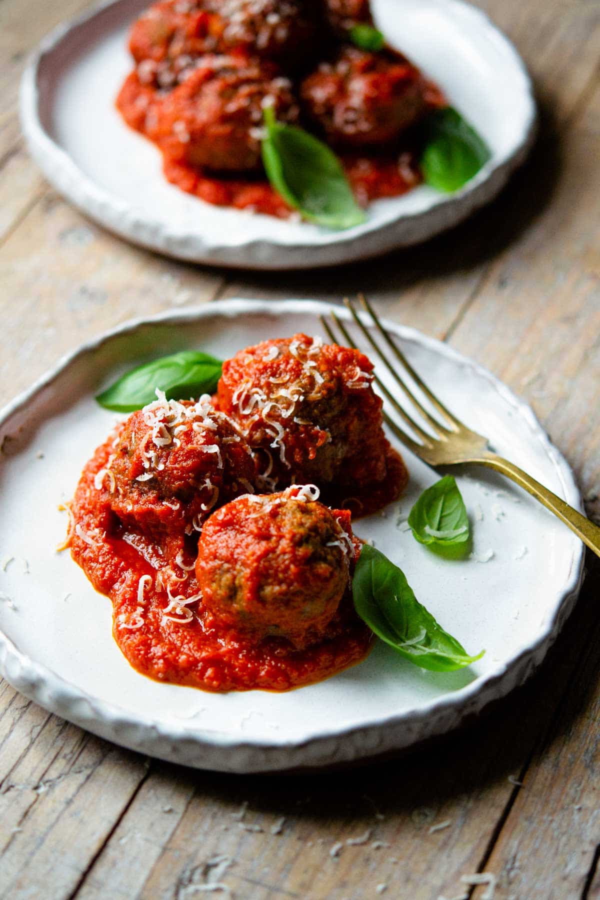 Three Italian meatballs on a rustic ceramic plate topped with fresh basil leaves