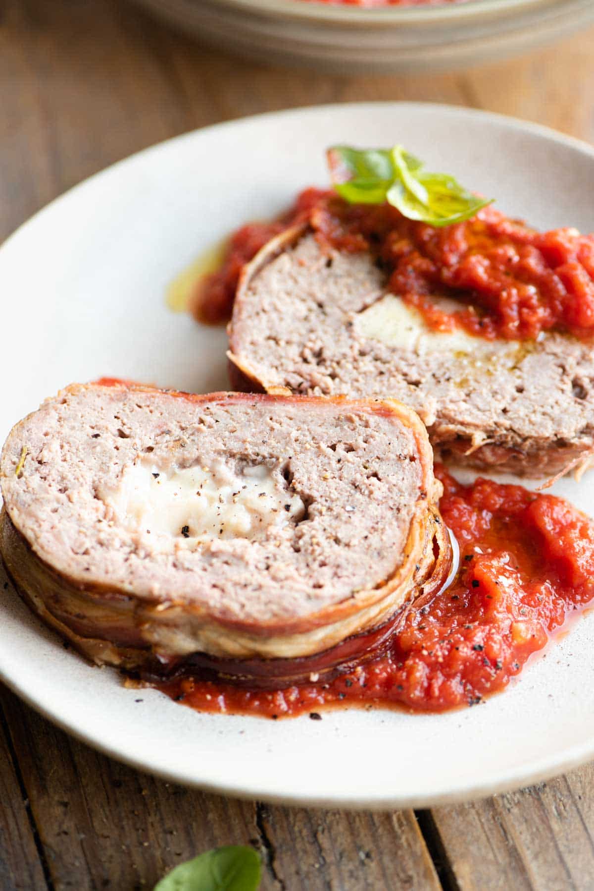 Two slices of cheese stuffed meatloaf on a plate with tomato sauce