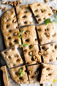 An overhead shot of a walnut focaccia cut into12 squares sprinkled with walnuts