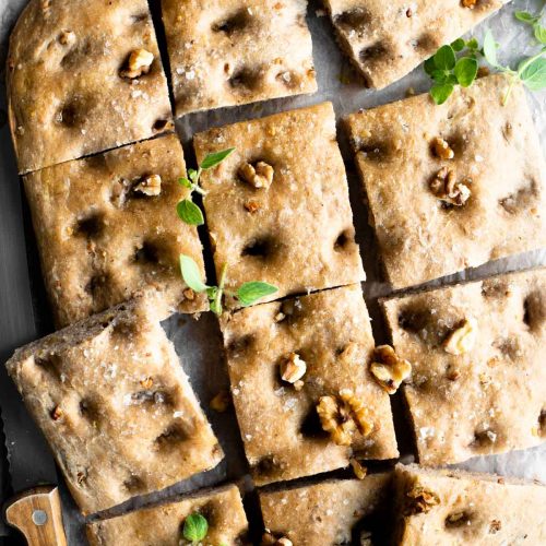 An overhead shot of a walnut focaccia cut into12 squares sprinkled with walnuts