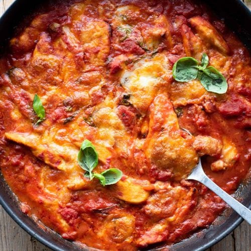 An overhead shot of a skillet with chicken baked in tomato sauce and topped with mozzarella