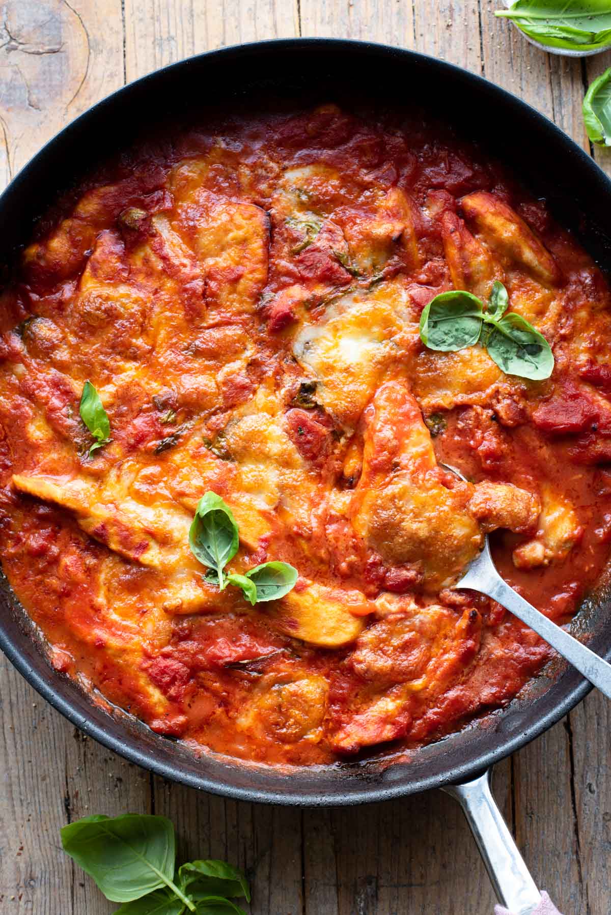 An overhead shot of a skillet with chicken baked in tomato sauce and topped with mozzarella