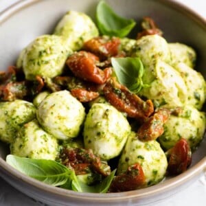 A close up of mozzarella bocconcini in a bowl with pesto and tomatoes